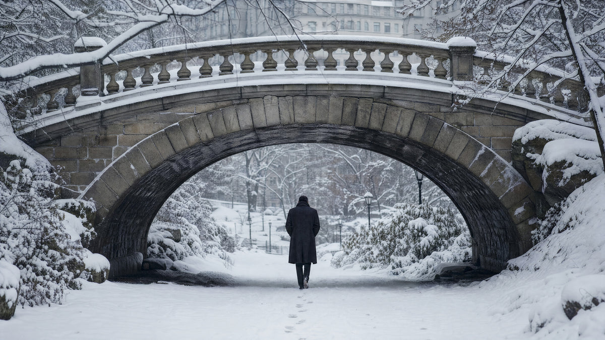 A stone bridge in a snowy park, a single figure in a dark overcoat walking away toward the city